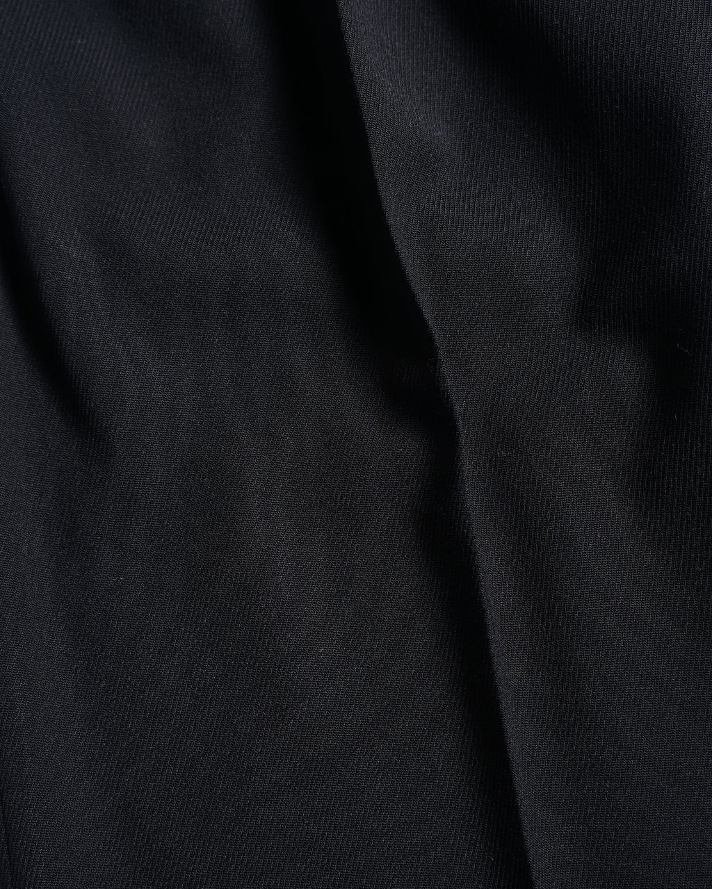 深みのあるブラックの生地表面と、落ち感によって生まれる陰影を捉えた素材アップ。細かな織りとしなやかな質感が確認できます。