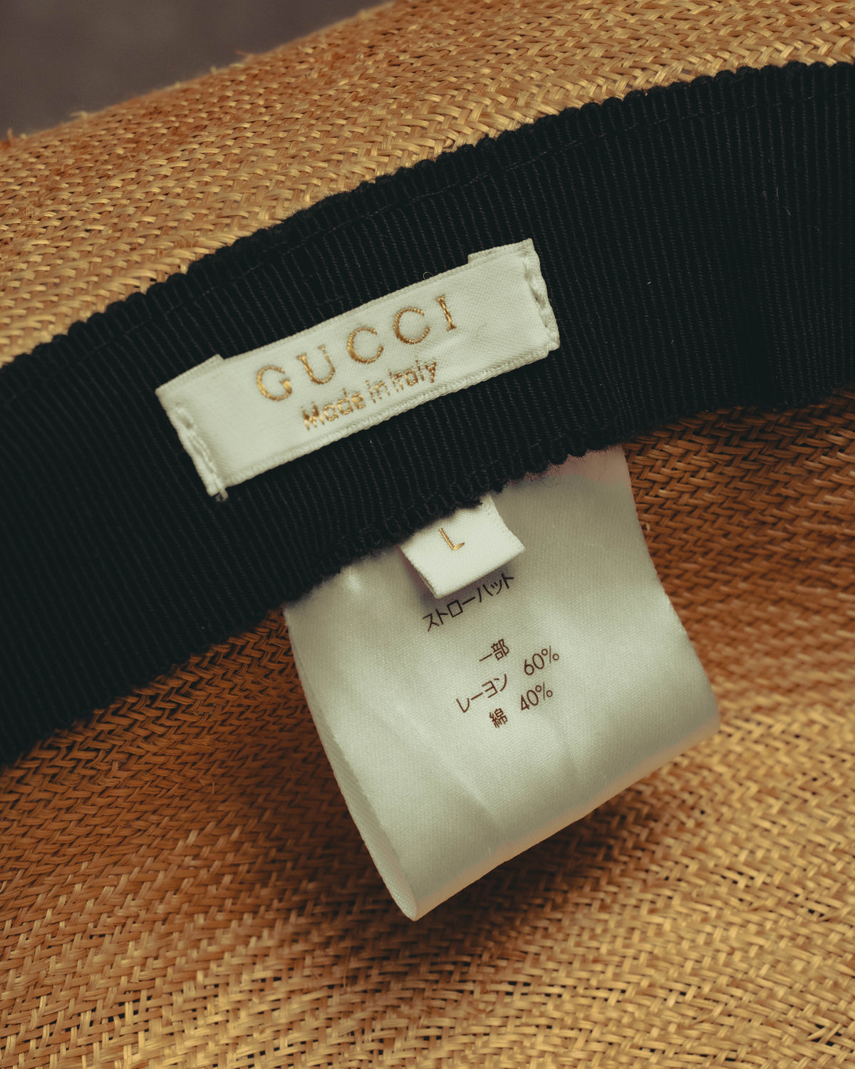 内側に配されたGUCCI・Made in Italy表記のブランドタグと、サイズLおよびレーヨン60％・綿40％の品質表示タグを確認できるカット。ブラックのグログラン調リボンとナチュラルな編み地も写しています。