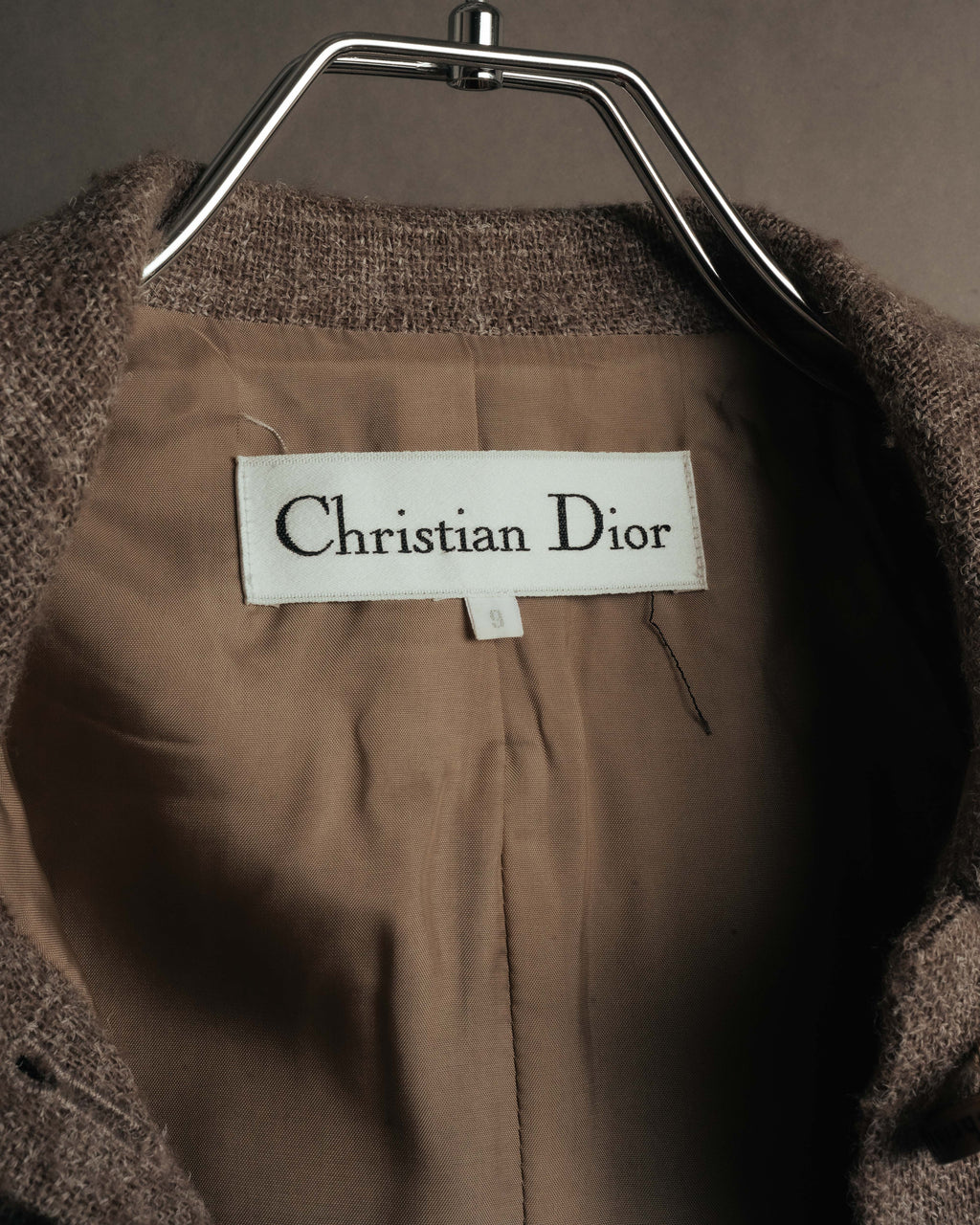総裏仕立ての内側に配された、セリフ書体の「Christian Dior」襟元織りタグ。茶系のキュプラ裏地とともに確認できる内側のディテールです。
