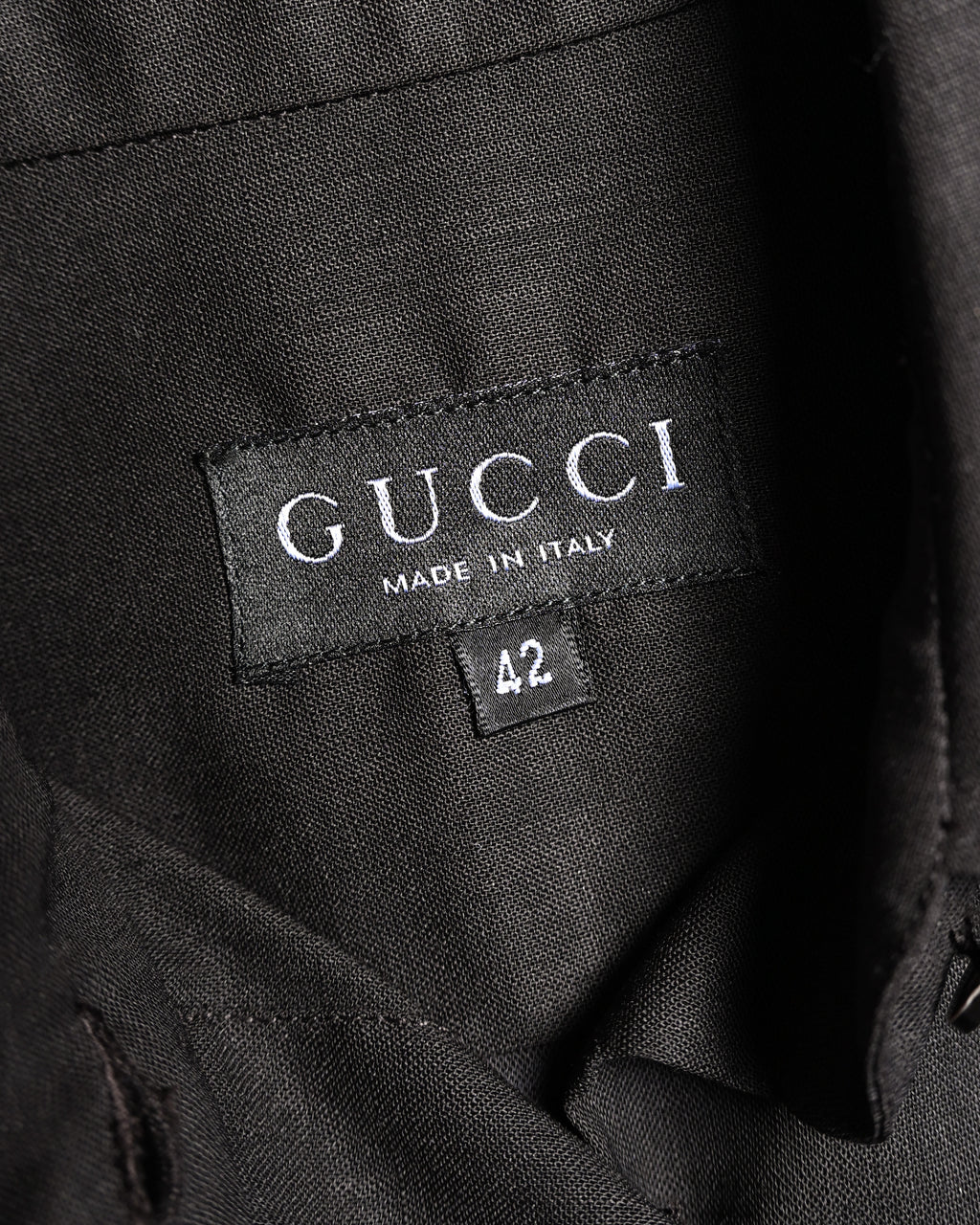 ブラックを基調としたセリフ体のGUCCIネックタグと、独立した42表記のサイズタグを捉えたカット。襟裏の細やかな織り目も確認できます。