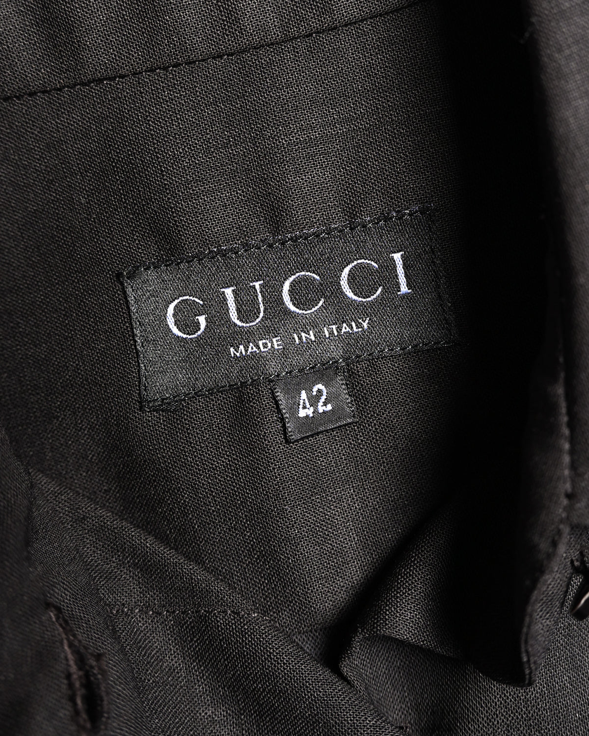 ブラックを基調としたセリフ体のGUCCIネックタグと、独立した42表記のサイズタグを捉えたカット。襟裏の細やかな織り目も確認できます。