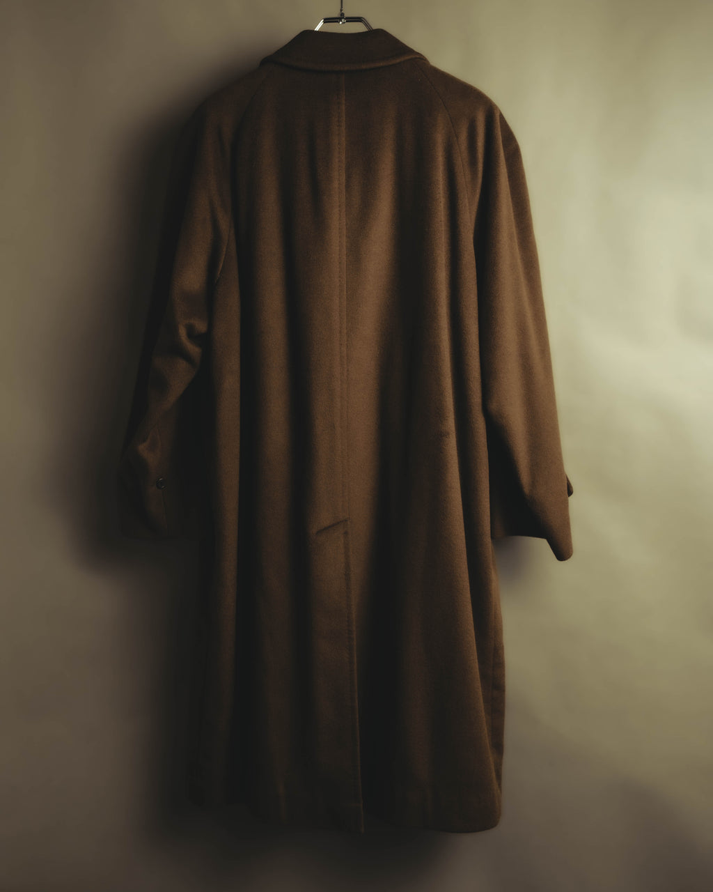 ブラウンのバルマカーンコートを背面から捉えた全体カット。裾のセンターベントと、ラグランスリーブから縦に落ちるストレート寄りのシルエットが確認できます。