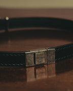 SAINT LAURENT PARISのロゴ刻印を配した、スクエア型メタル留め具（クラスプ）のディテール。ブラックレザーストラップの均整の取れたステッチも確認できるカット。
