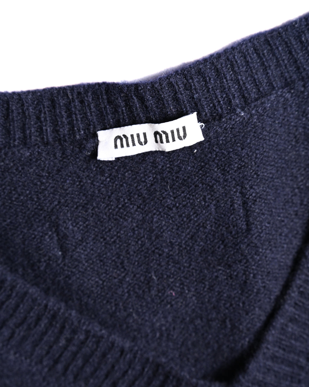 背面の襟下に配された、ブラックを基調とした「miu miu」ロゴパッチのディテールカット。周囲にはネイビーの細やかな編み地とリブ編みが確認できます。