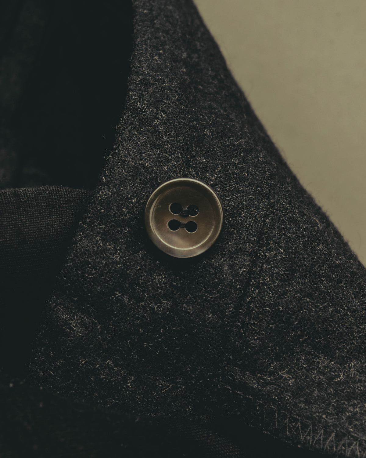 ウエスト両脇に配された、無刻印の四つ穴ボタンを捉えたディテールカット。深いチャコールグレーのウール地に穏やかな起毛感が見られます。