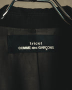 総裏仕立ての内側、首元に配された「tricot COMME des GARÇONS」ブランドタグのクローズアップ。黒地に白文字で織りネームが確認できるカット。