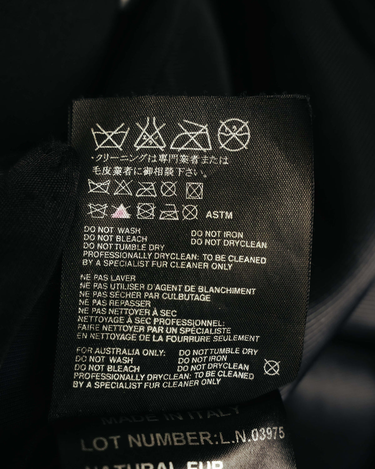 クリーニング専門店によるドライクリーニング指定を記した、複数言語表記の洗濯表示タグ。下部にはイタリア製表記とロットナンバーのタグが重なって見える。