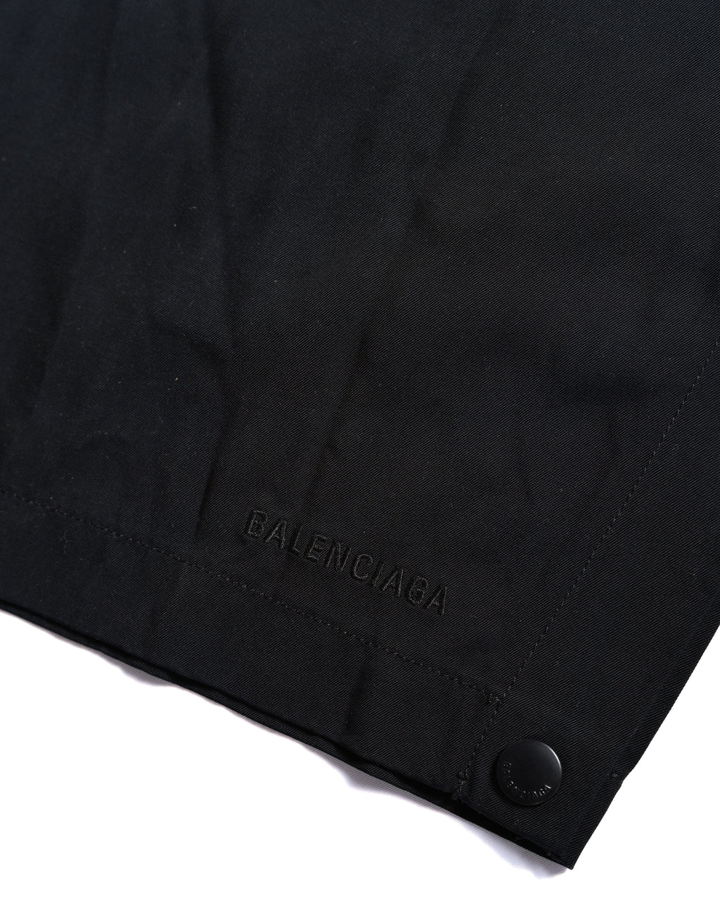 裾側に配されたブラックの刻印入りスナップボタンと、同色のBALENCIAGAロゴ刺繍を捉えたディテールカット。ボタンを外してスリットを作れるサイド仕様の裾部分です。