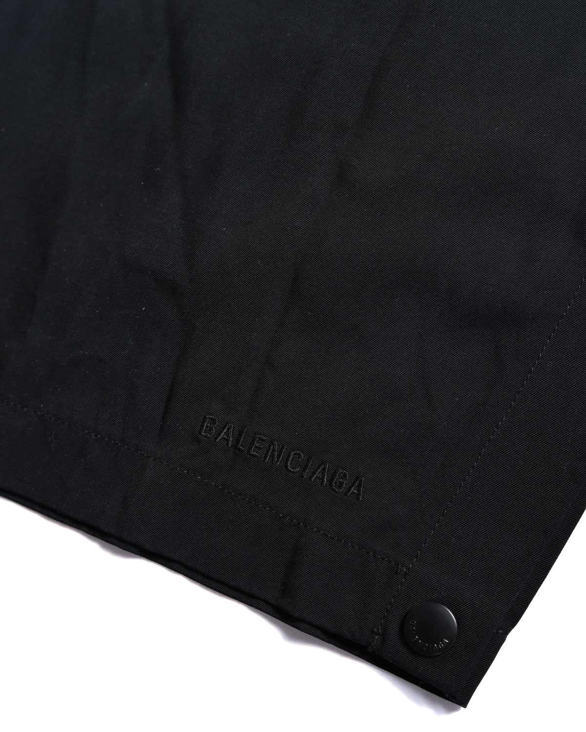 裾側に配されたブラックの刻印入りスナップボタンと、同色のBALENCIAGAロゴ刺繍を捉えたディテールカット。ボタンを外してスリットを作れるサイド仕様の裾部分です。