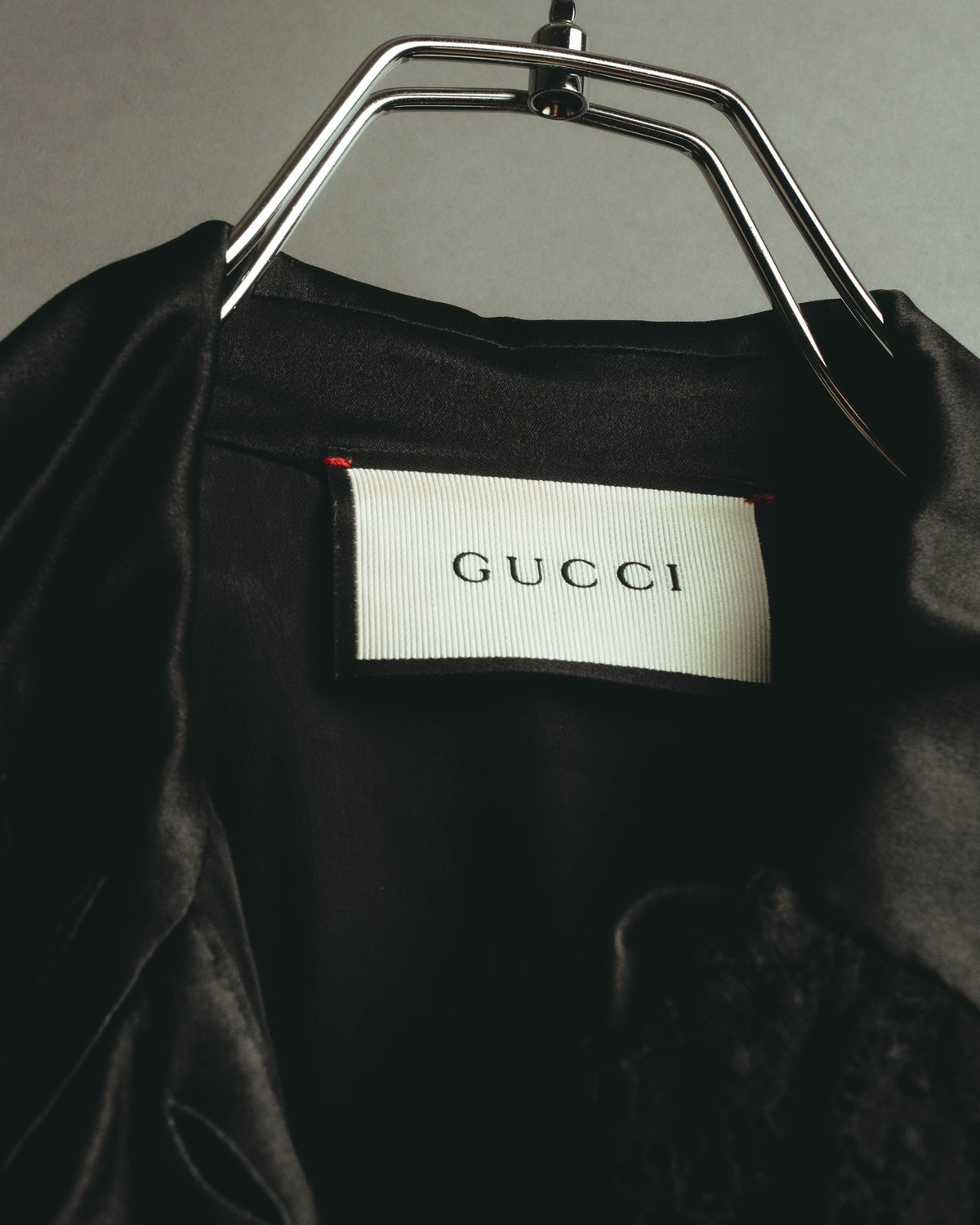 首元に配されたGUCCIロゴ入りのブランドタグを写したカット。ブラックの生地に白地の織りタグと赤い縫い留めが確認できます。
