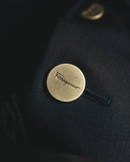深いブルーブラックのウール地に配された、Ferragamoの筆記体ロゴ入りメタルボタンのディテールカット。フロントに用いられたボタンの刻印と質感が確認できます。