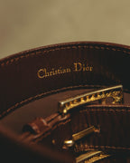 ダークブラウンの帯材内側に施された、セリフ体の「Christian Dior」金色箔押し表記を捉えたカット。端正なステッチと、手前にピン式バックルの裏側が写ります。