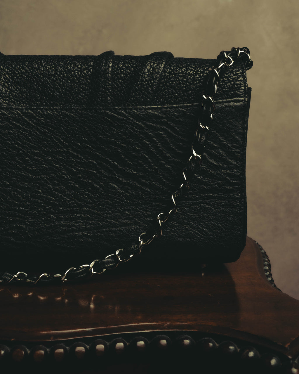 ブラックレザーを編み込んだシルバーカラーのチェーンショルダーストラップを、本体側面とともに捉えたディテールカット。チェーンの光沢と細かな凹凸が連なるブラックレザーの質感が確認できます。