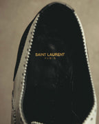 ブラックのインソール中央に入る、ゴールドカラーの「SAINT LAURENT PARIS」ロゴ刻印を写したディテールカット。履き口周囲にはホワイトレザーとブローギングのパーフォレーションが確認できます。