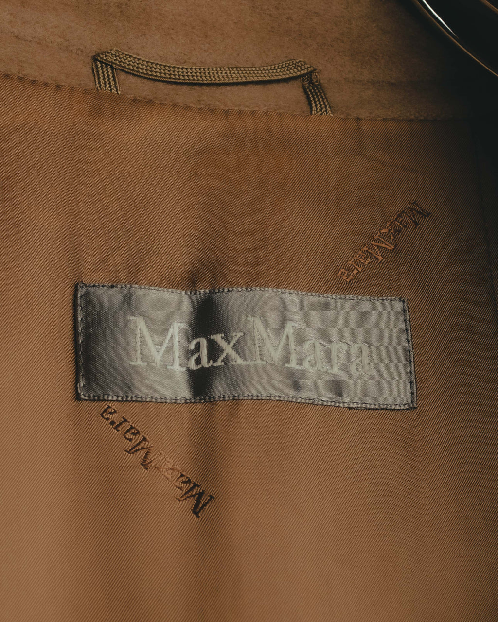 シルバーグレーのサテン地に白糸でMaxMaraを織り込んだネームタグのカット。総裏ライニングには同系色のロゴが織り込まれています。