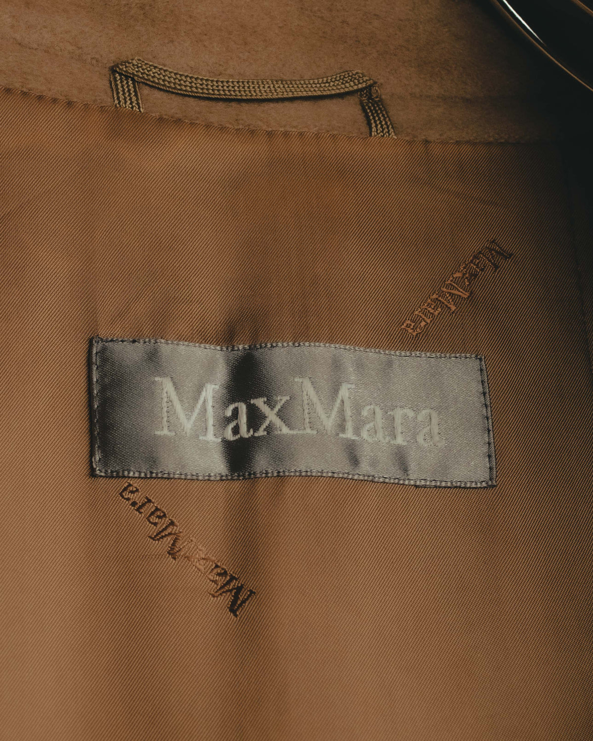 シルバーグレーのサテン地に白糸でMaxMaraを織り込んだネームタグのカット。総裏ライニングには同系色のロゴが織り込まれています。