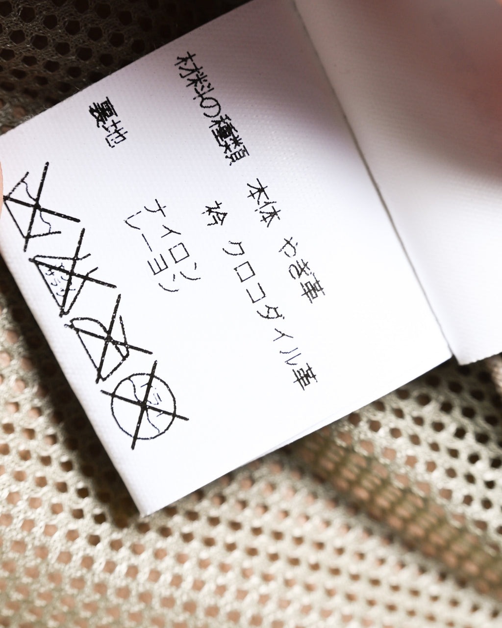 ナイロンを含む素材表記と洗濯表示が確認できる内側の品質表示タグ。メッシュ状の裏地を背景に捉えたタグのクローズアップです。
