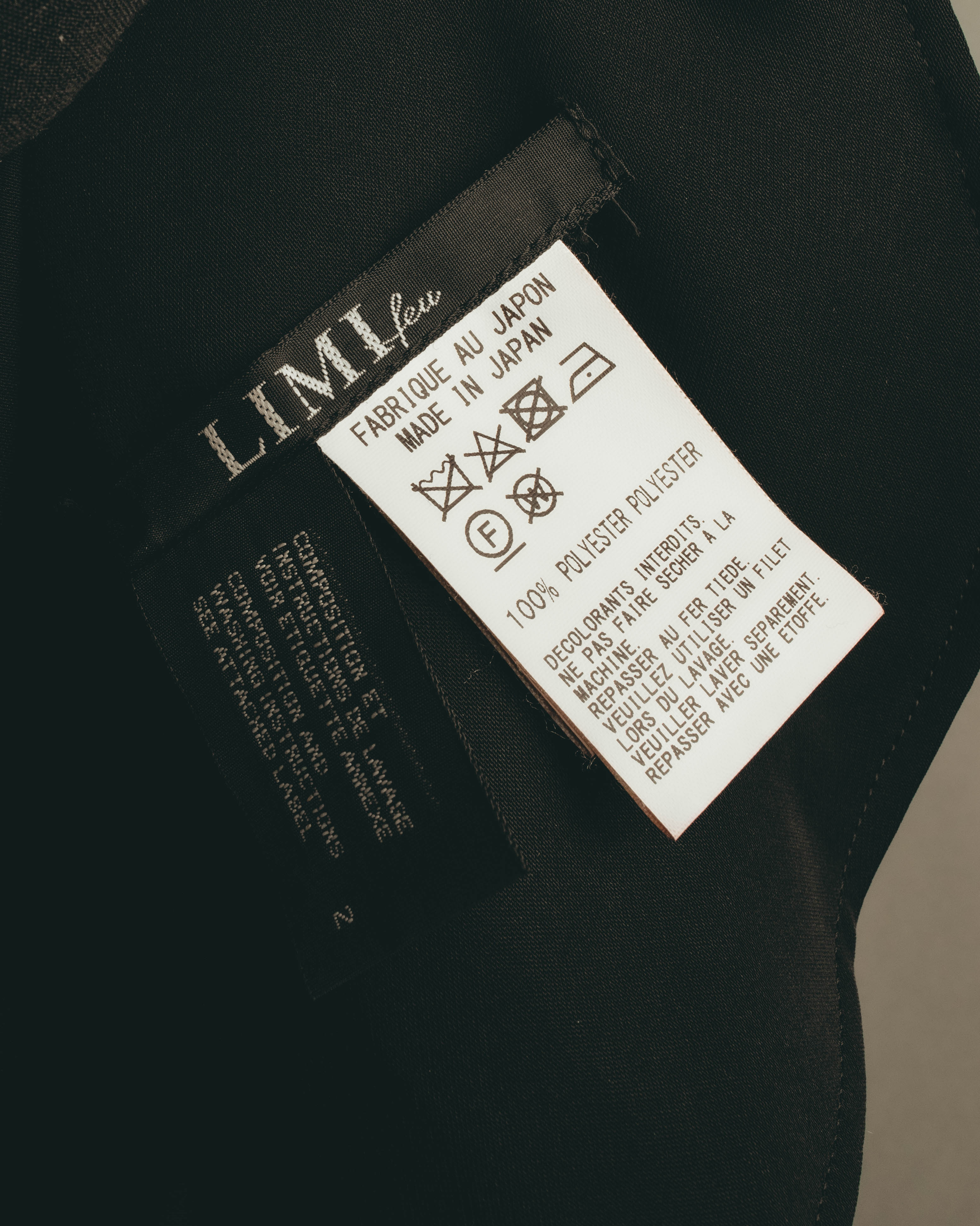 内側に配されたLIMI feuのブランドタグと洗濯表示タグのクローズアップ。タグ表記で日本製、ポリエステル100パーセントを確認できるカット。