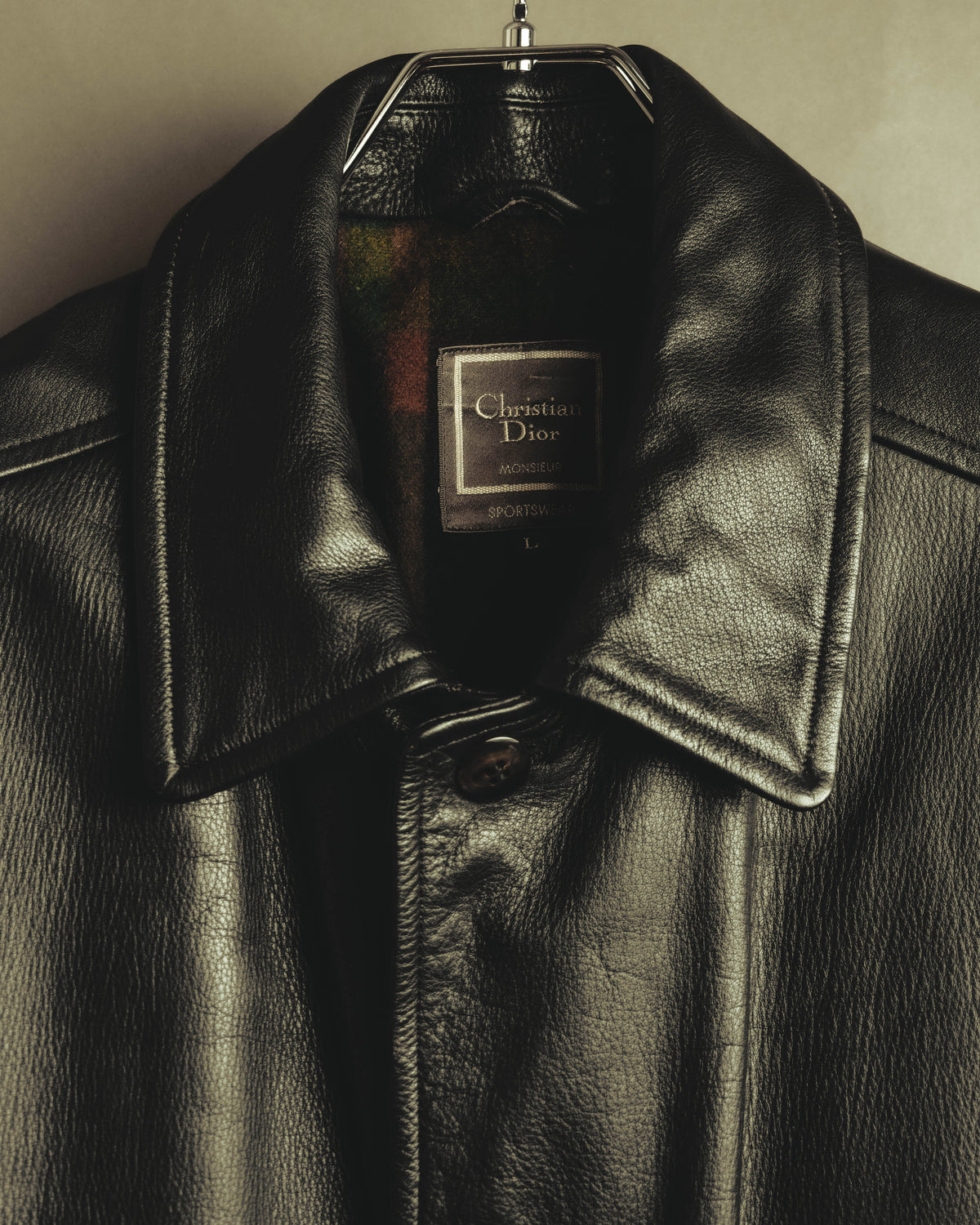 大ぶりな襟元に配された Christian Dior Monsieur Sportswear の織りネームと、独立したLサイズ表記を捉えたカット。フロントの4穴ボタンと、内側から覗く多色チェック柄の起毛生地も確認できます。