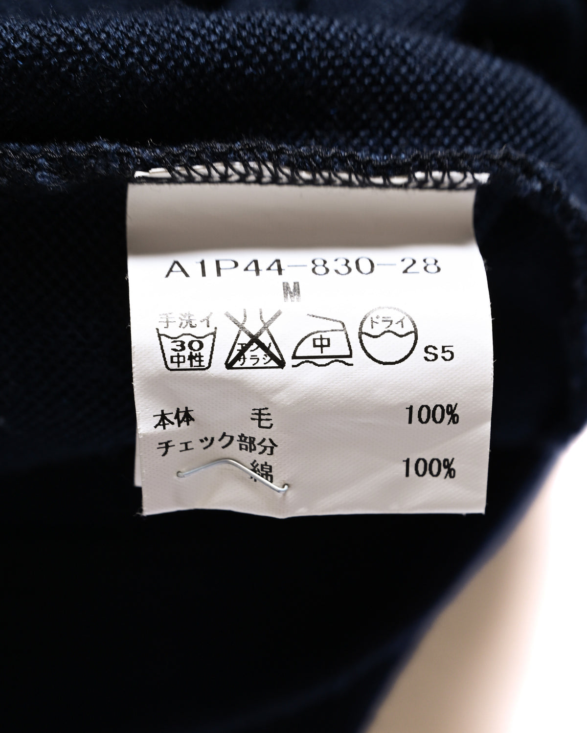内側の洗濯表示タグに、素材表記として本体ウール100%・チェック部分コットン100%を記載したカット。品番「A1P44-830-28」とサイズMも確認できます。