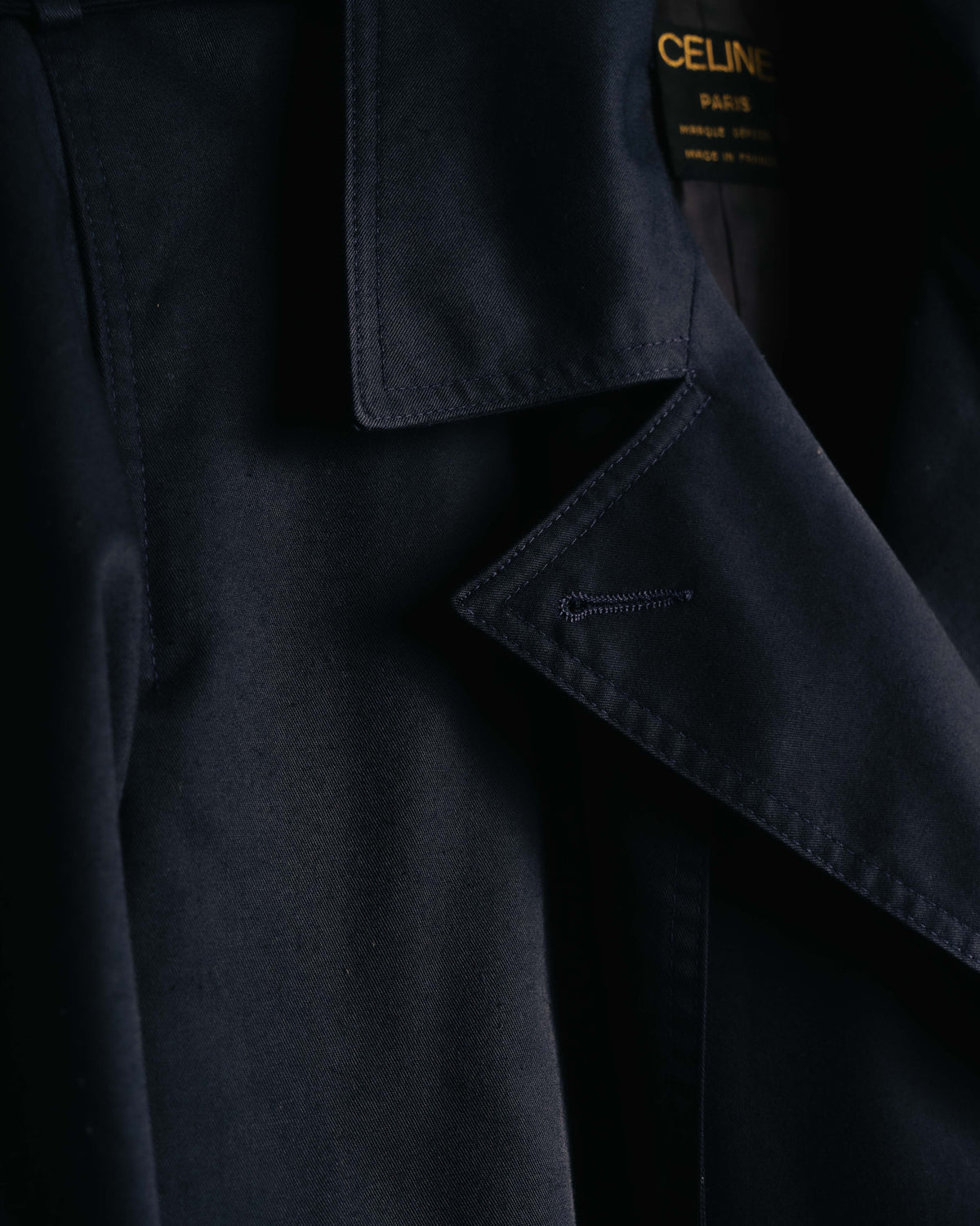 黒地に金文字でCELINE PARIS、MARQUE DÉPOSÉE、MADE IN FRANCEと織られた首元の旧タグと、ダークネイビーのラペルを捉えたカット。