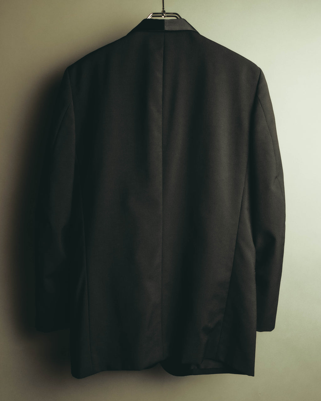 ブラック系ウール地のジャケットを背面から捉えた全体カット。構築的な肩周りからすっきりとした身頃へ続くラインと、背面中央の縫い目が確認できます。