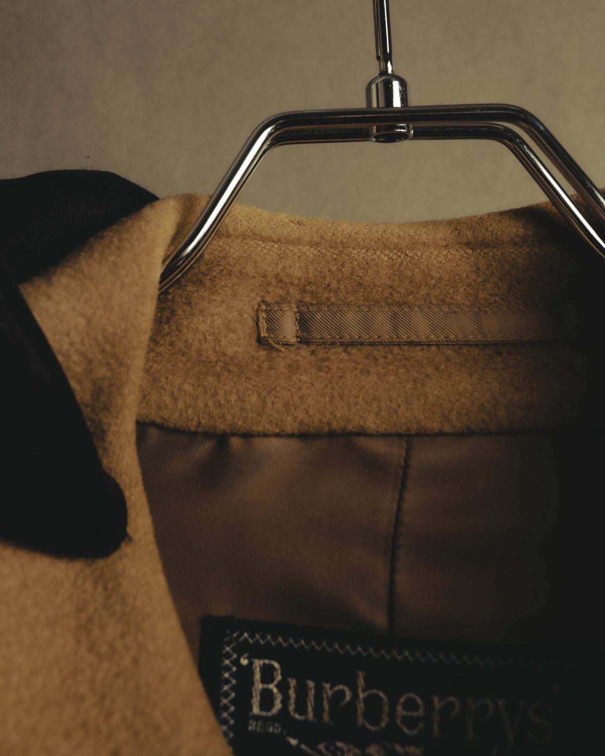 内側に配された旧来のBurberrysロゴタグとハンガーループを捉えたカット。キャメルベージュの起毛した表地と滑らかな裏地も確認できます。