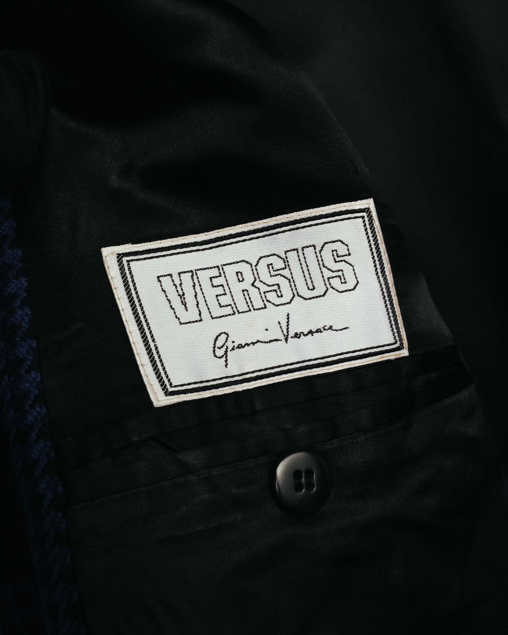 白地にアウトライン書体のVERSUSと筆記体のGianni Versaceを組み合わせた織りタグ。ブラックの総裏地と内ポケットのボタンも確認できる内側のカット。