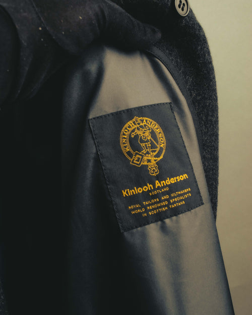 内側のブラックからダークグレー系の総裏地に配された、Kinloch Andersonのブランド織りネーム。上部には比翼仕立ての内側に隠れる黒い4穴ボタンも確認できます。