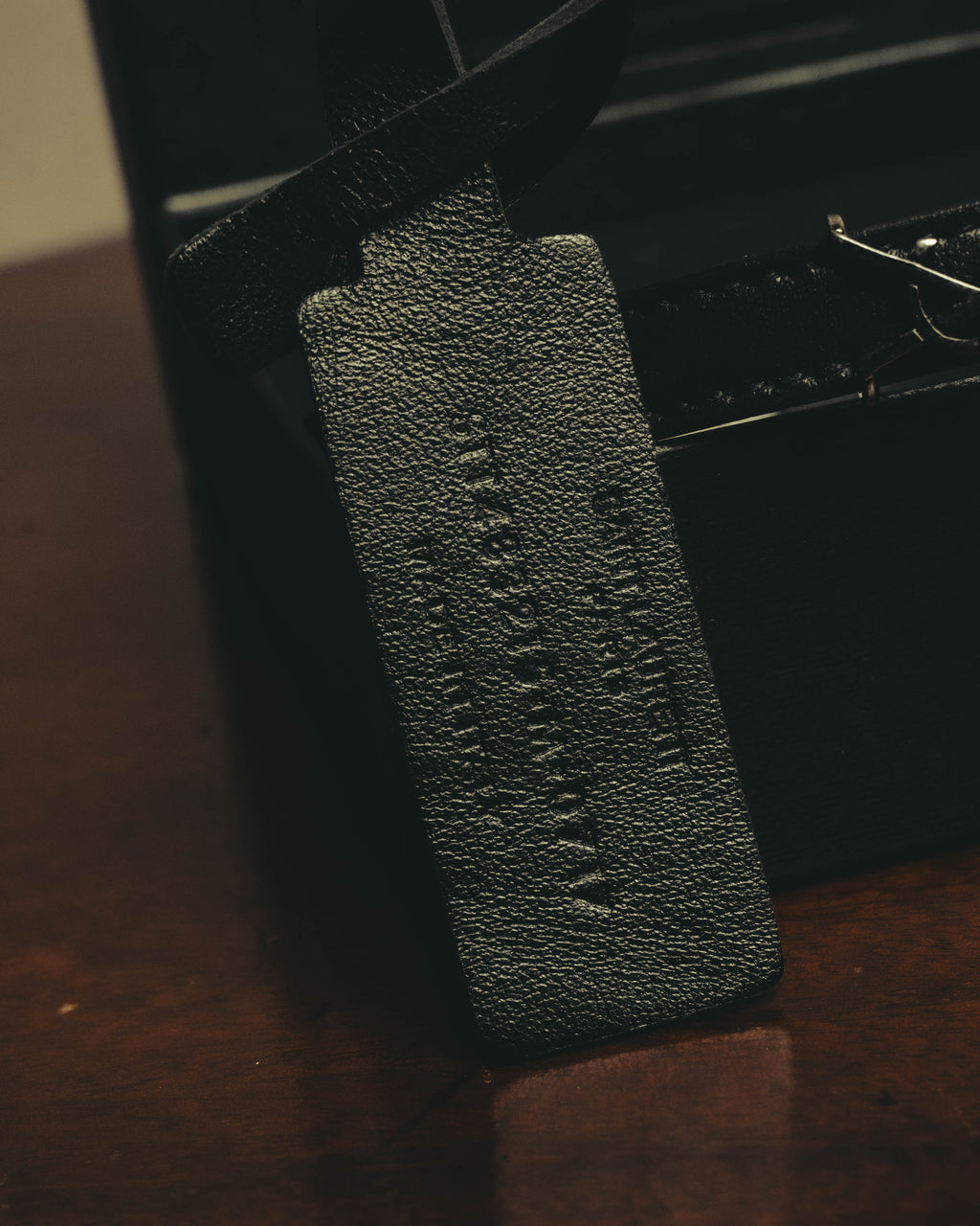 SAINT LAURENT PARISの刻印が施されたブラックレザーストラップと、端部の留め具（クラスプ）を捉えたディテールカット。レザーのシボ感とブラックで統一された仕上がりが確認できます。