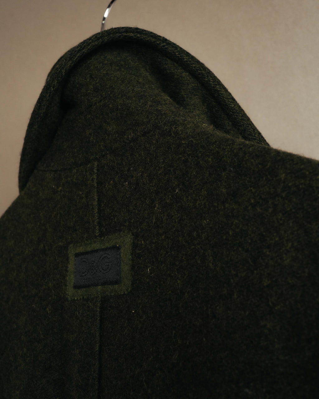 背面上部に配されたD&Gロゴパッチを捉えたディテールカット。ダークチャコールの繊細な起毛感を伴うウール混生地と、背中心の直線的なラインも確認できます。