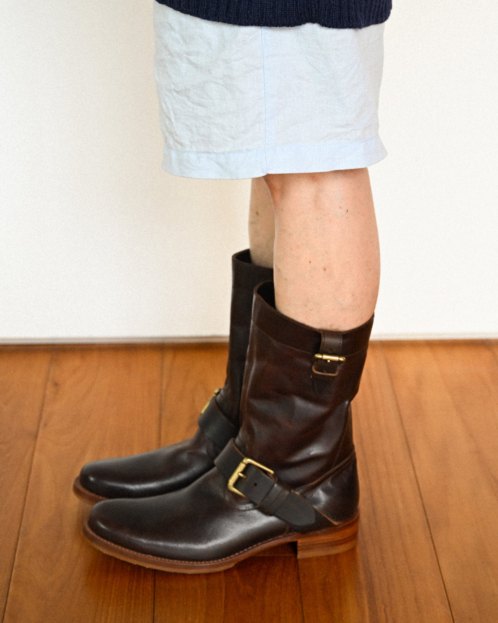サックスブルーのショートパンツにダークブラウンのプレントゥ エンジニアブーツを合わせた着用カット。甲部分と筒上部の真鍮製バックルベルト、すっきりとした筒周りのバランスが確認できます。
