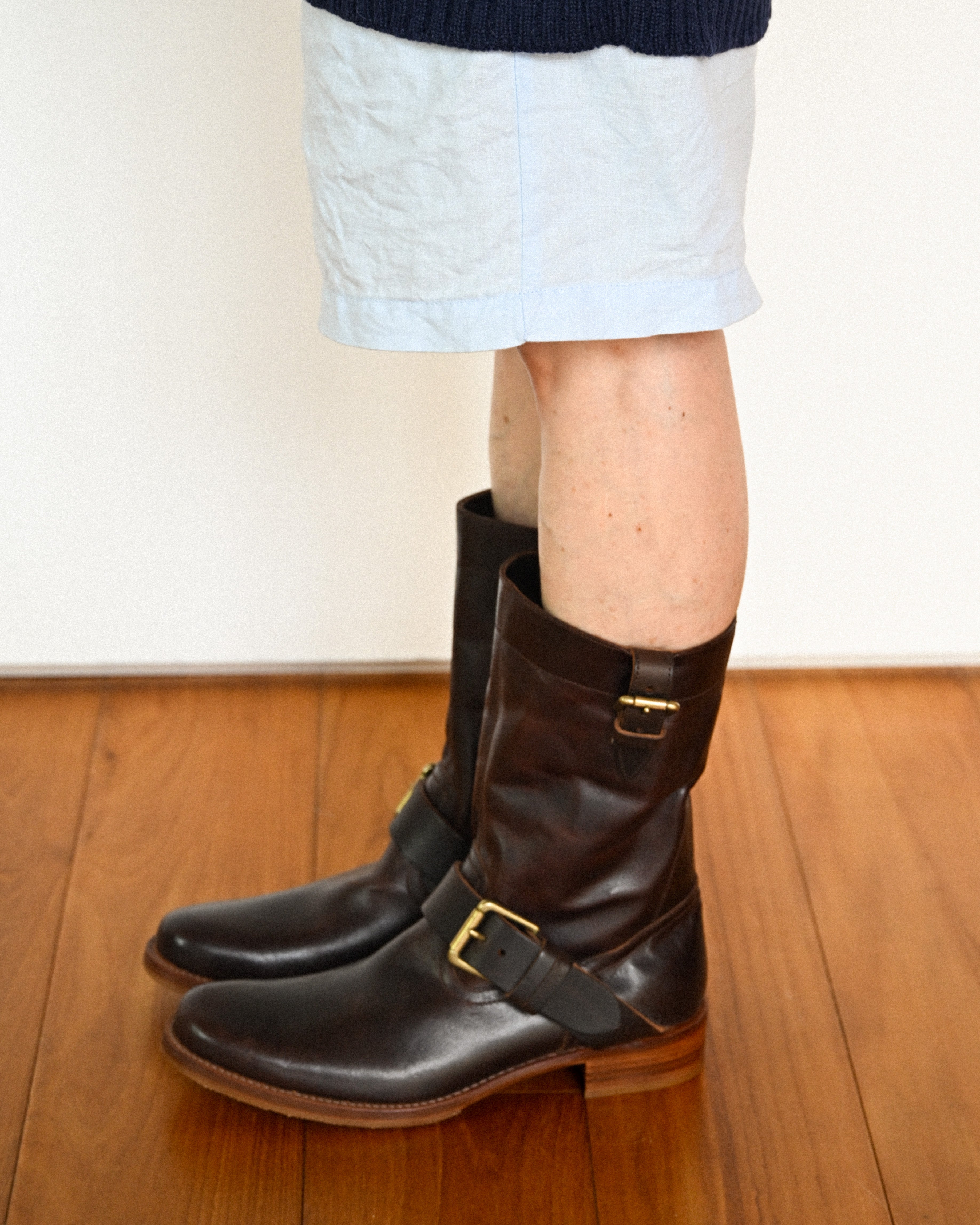 サックスブルーのショートパンツにダークブラウンのプレントゥ エンジニアブーツを合わせた着用カット。甲部分と筒上部の真鍮製バックルベルト、すっきりとした筒周りのバランスが確認できます。