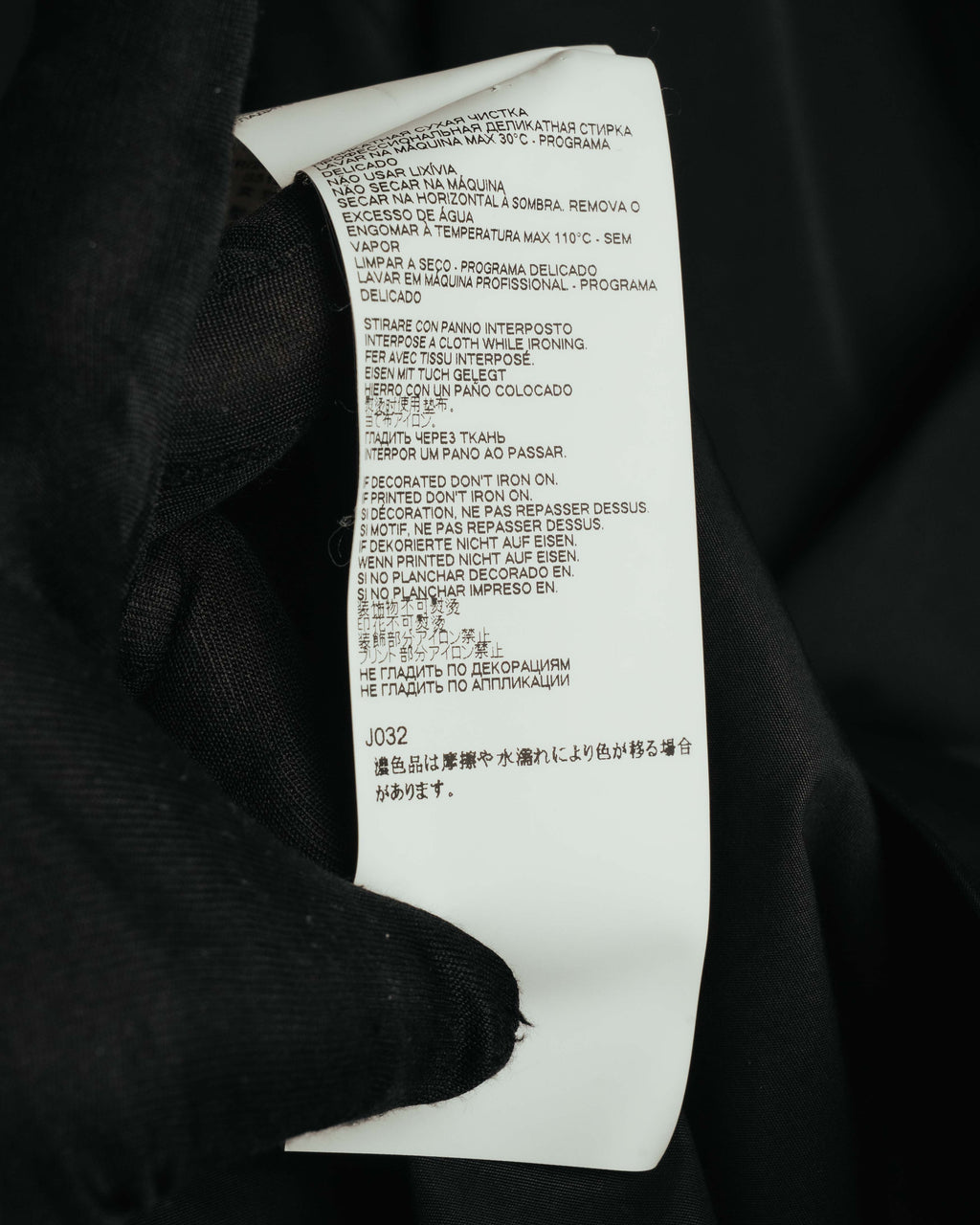 多言語のケア表記と品番J032が確認できる品質表示タグのクローズアップ。洗濯・アイロンに関する取り扱い表示を捉えたカット。