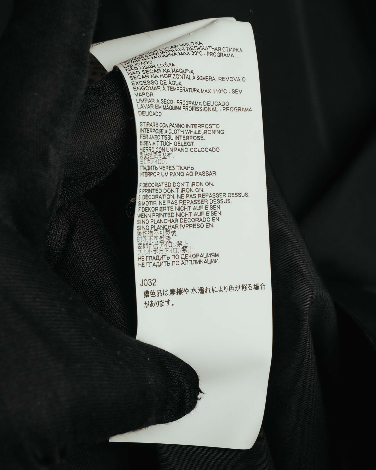 多言語のケア表記と品番J032が確認できる品質表示タグのクローズアップ。洗濯・アイロンに関する取り扱い表示を捉えたカット。