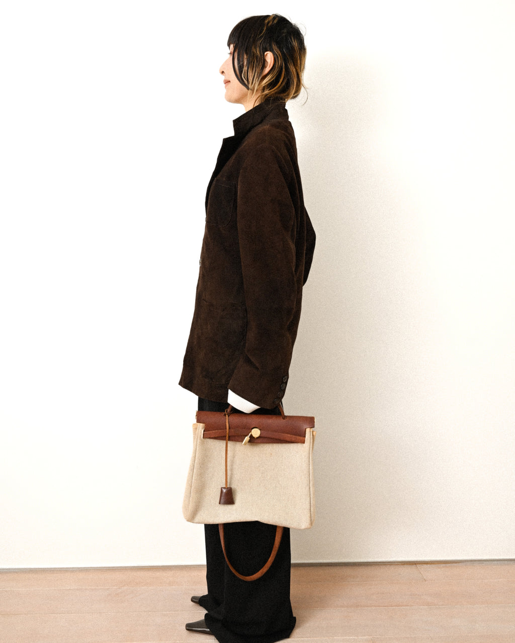 ダークブラウンの起毛素材を用いたジャケットを横から捉え、肩から裾へ素直に落ちるラインと腰を覆う着丈を確認できる着用カット。袖口には四つのボタンが並んでいます。