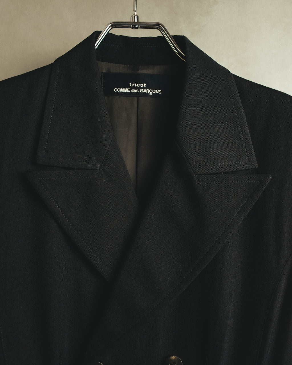 端正なノッチドラペルと、襟元に配された「tricot COMME des GARÇONS」ネームタグを捉えたディテールカット。ブラックの毛100パーセント表地と総裏仕立ての内側が確認できます。