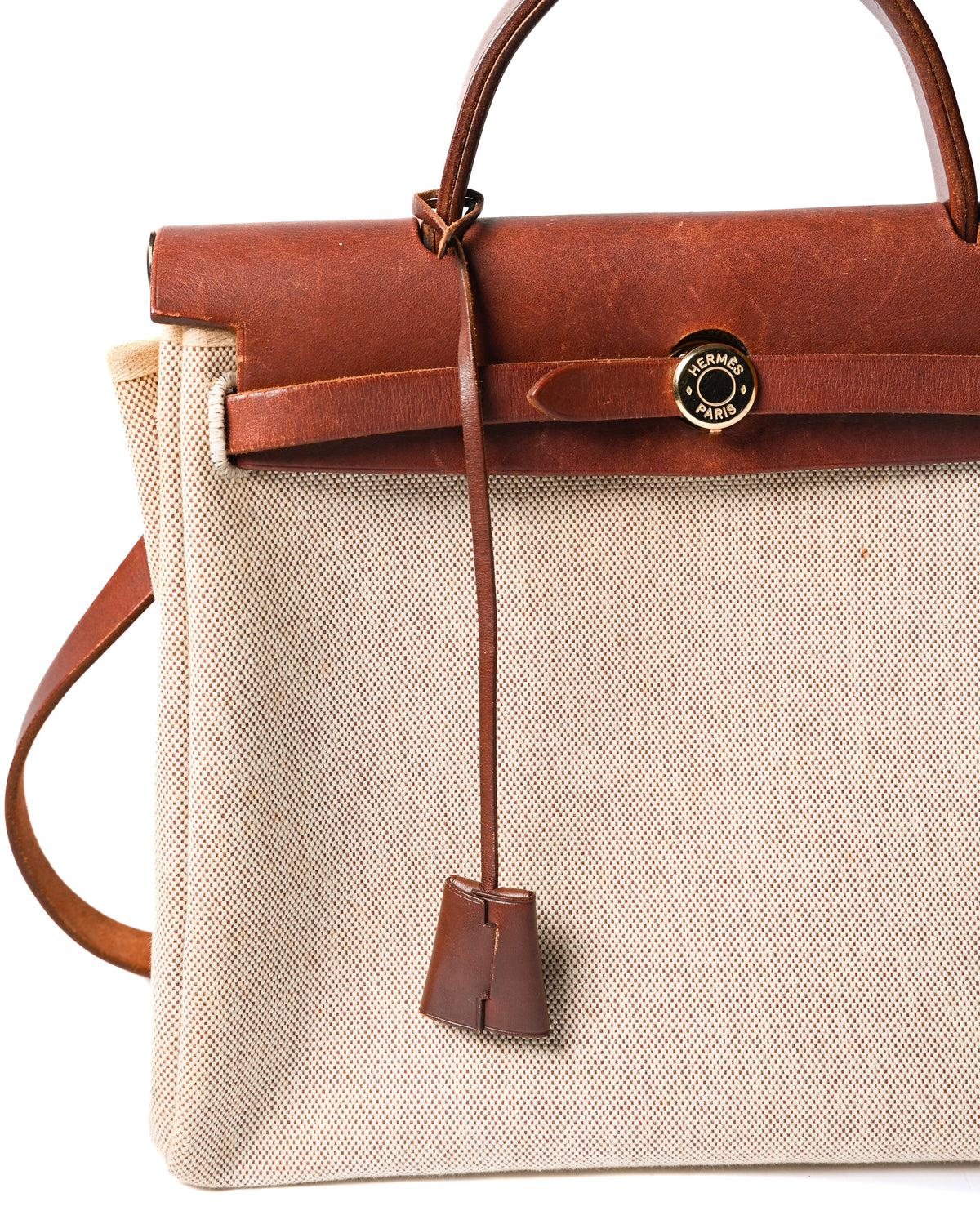 フロントのベルトを通して留める、HERMÈS PARIS刻印入りゴールドカラーのセリエ金具を捉えた正面ディテール。深いブラウンのレザートップパーツから、クロシェットが縦に垂れる仕様です。