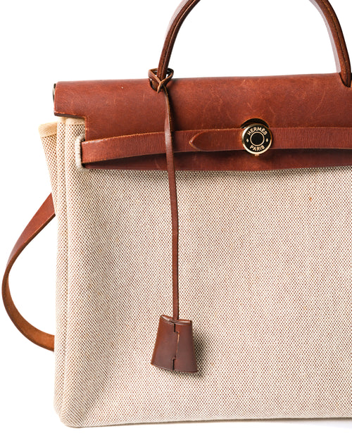 フロントのベルトを通して留める、HERMÈS PARIS刻印入りゴールドカラーのセリエ金具を捉えた正面ディテール。深いブラウンのレザートップパーツから、クロシェットが縦に垂れる仕様です。