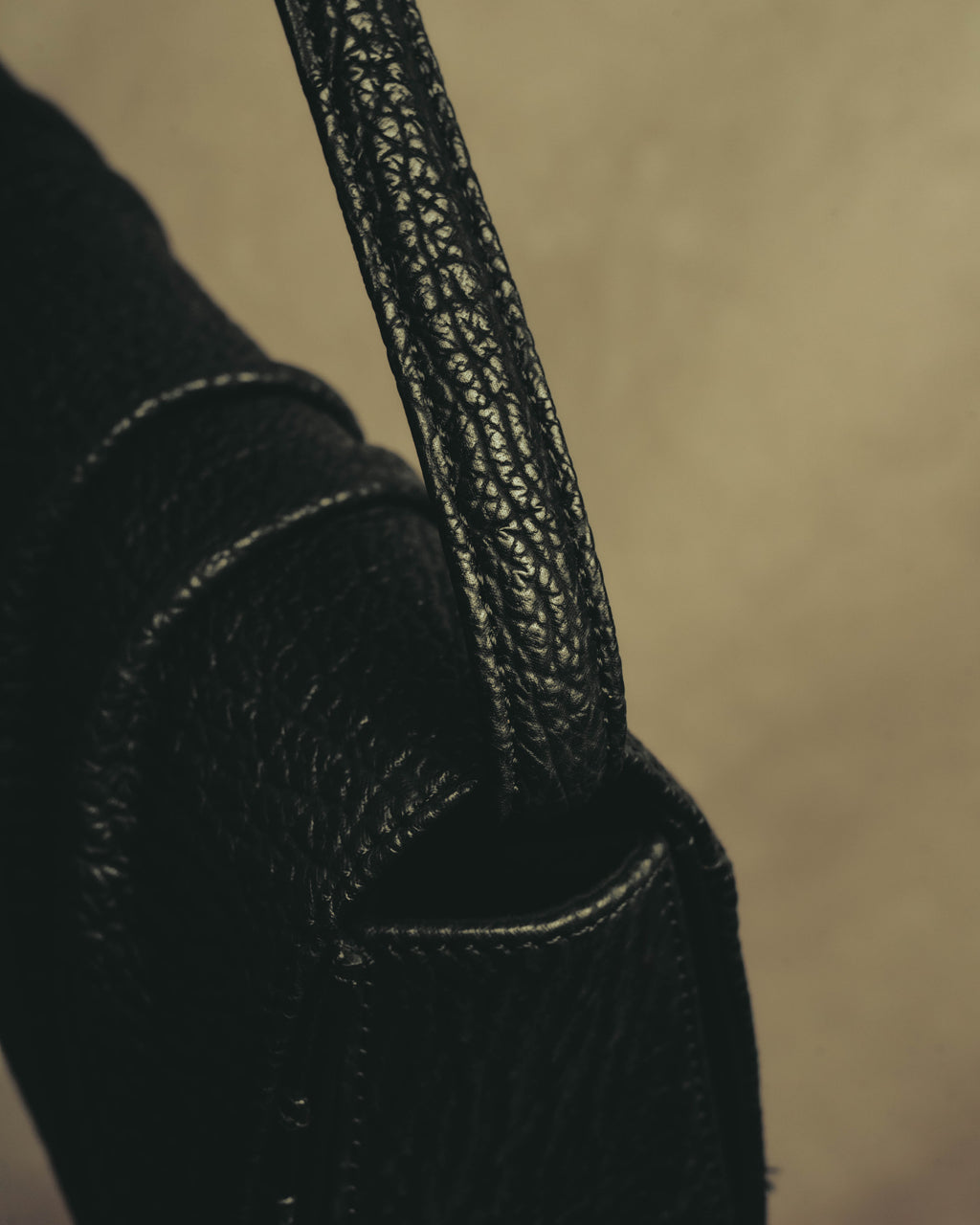 ブラックレザーのショルダーストラップと、本体側面の付け根を捉えたディテールカット。細かな凹凸が連なるレザーの質感と縁のステッチが確認できます。