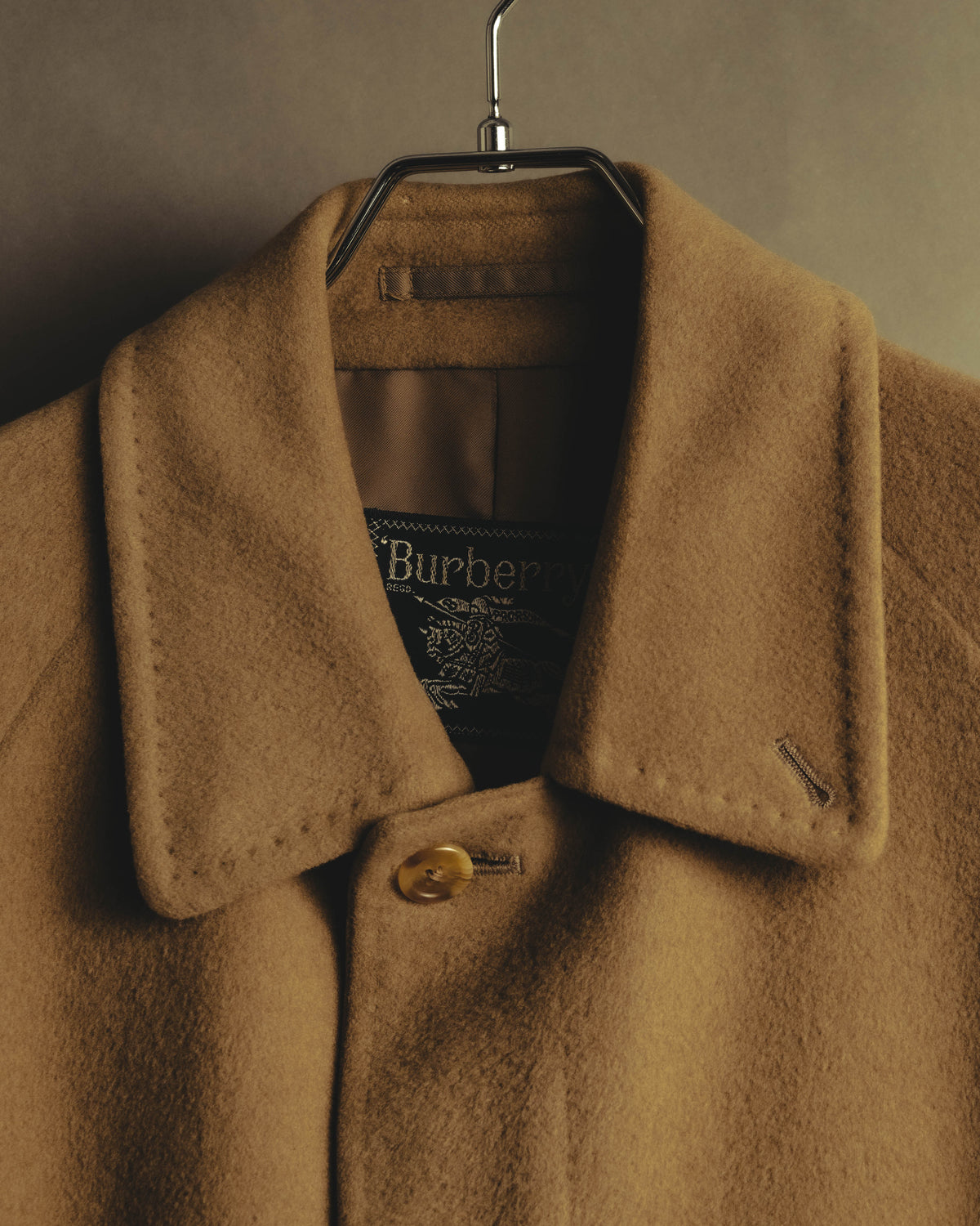 キャメルベージュの起毛感ある襟元に、旧来のBurberrysロゴと騎士図案入りのタグ、首元のボタンを収めたディテールカット。
