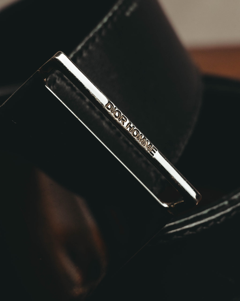 鏡面仕上げのプレートバックル上部に配された、DIOR HOMME刻印のディテール。ブラックのレザーベルトとシルバー系金属色のコントラストが確認できます。