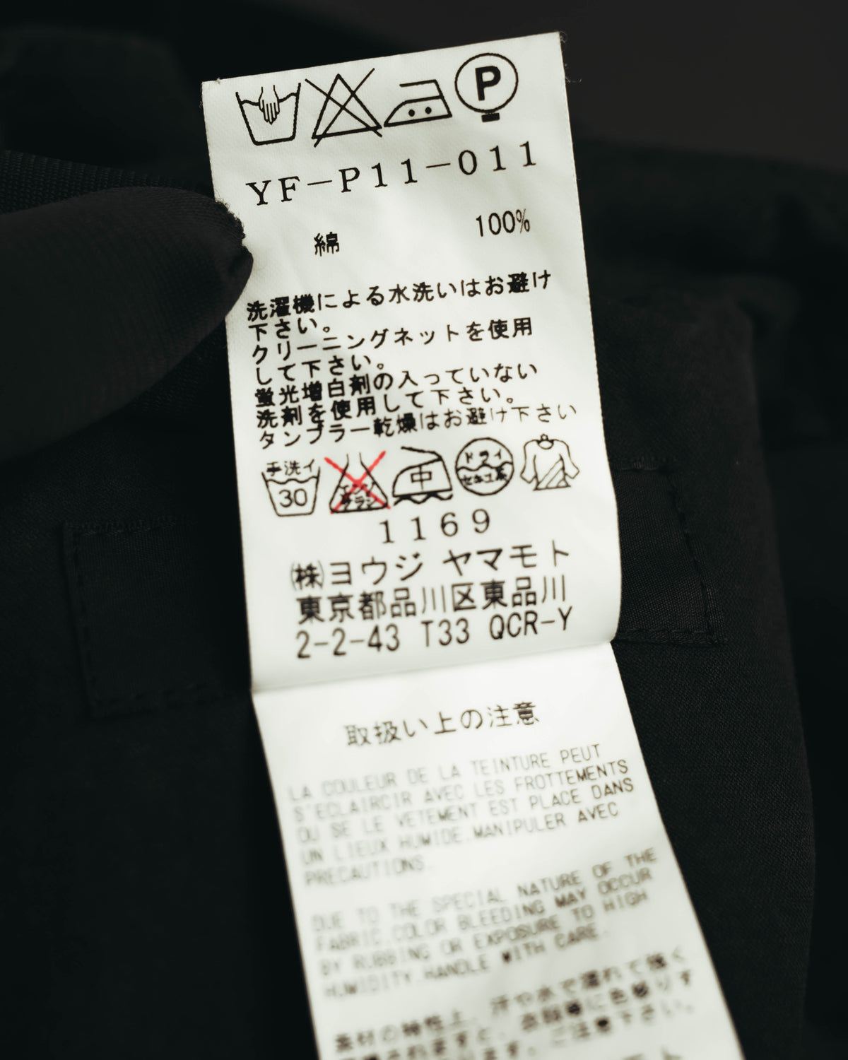内側に配された洗濯表示タグのカット。品番「YF-P11-011」、素材表記「綿 100%」およびサイズ表記「1」が確認できます。