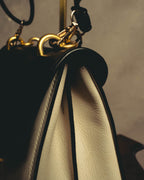 サイドのアコーディオン状マチ上部に配された、ショルダーストラップ接続用のゴールドカラーDリングとナスカンのディテールカット。ボーンカラーのシボ革とブラックのトリミングのコントラストも確認できます。