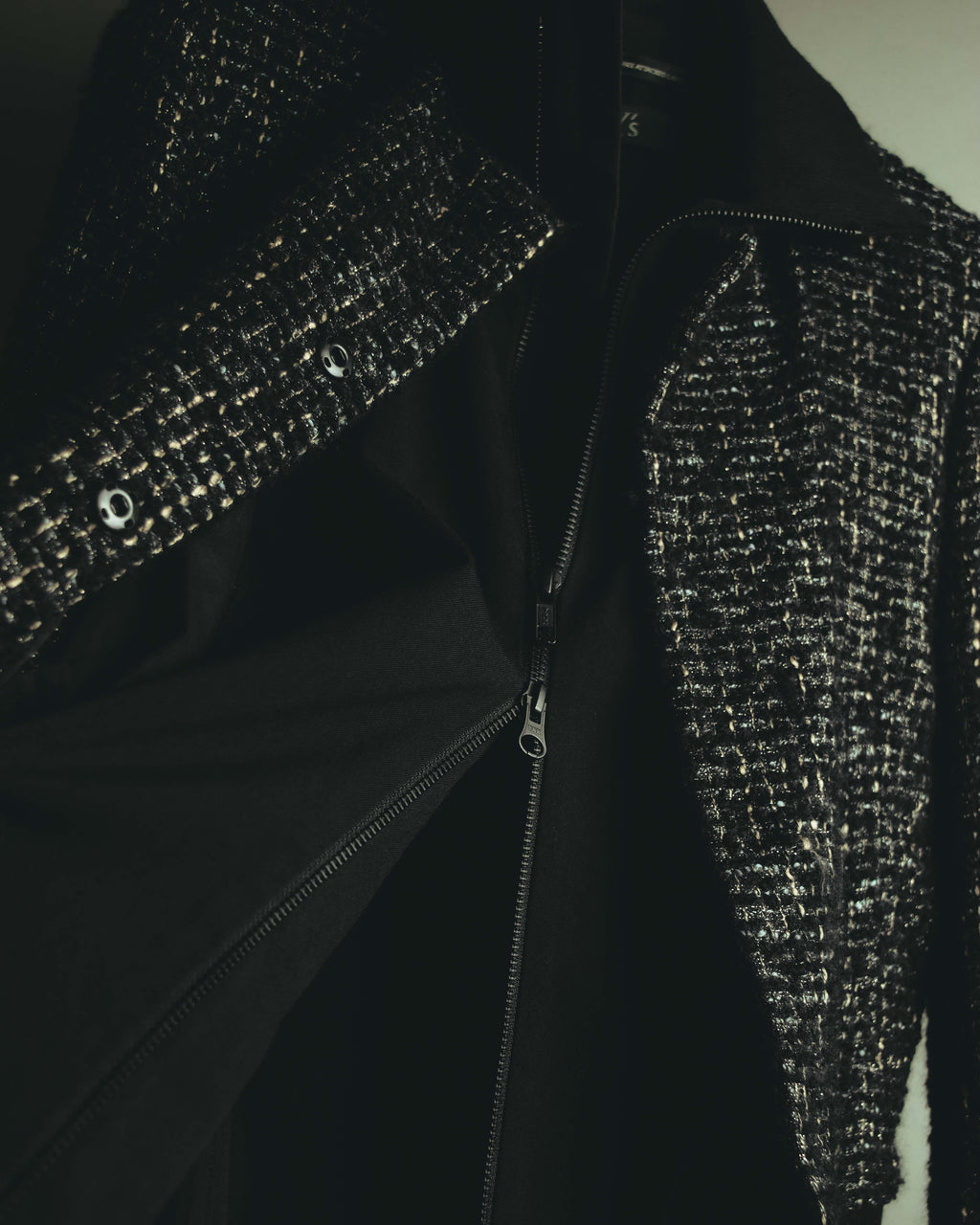 ブラックベースのツイード上身頃を開いた内側に、ブラックの身頃と上下から開閉するダブルスライダー式ジッパーを配したディテールカット。ツイードの織りと内側のジップアップ構造の重なりが確認できます。