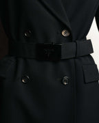 共布ベルトに配された、PRADA MILANO DAL 1913の文字と紋章が刻まれた艶を抑えた黒系メタルの大型バックル。ダブルブレストのボタンとフラップポケットも併せて確認できるディテールカット。