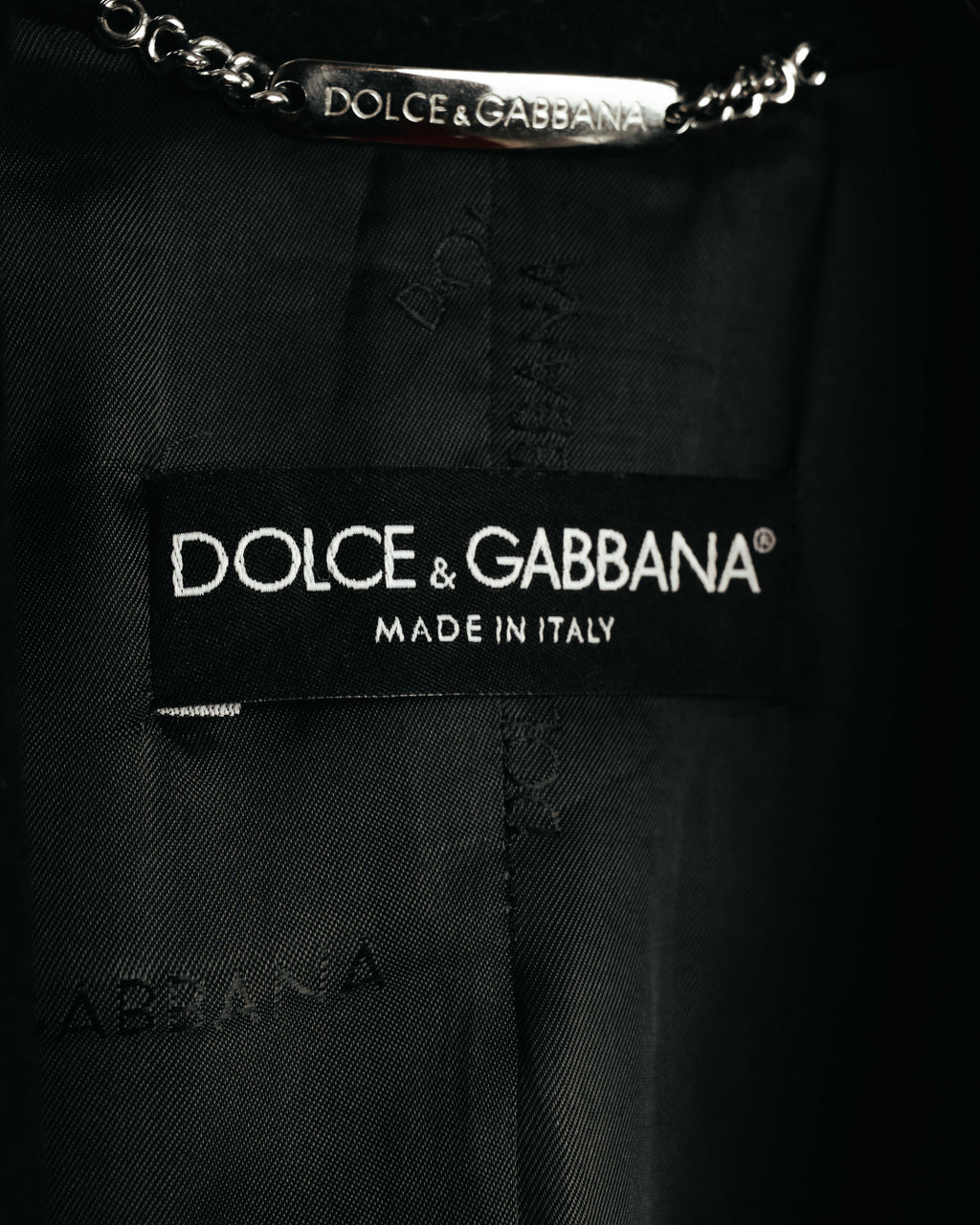 内側に配された、DOLCE & GABBANAのブランドネーム刻印入りメタルチェーンハンガーループと「MADE IN ITALY」表記の首元織りタグ。総裏地にはブランドネームを織り込んだジャカード柄が確認できます。