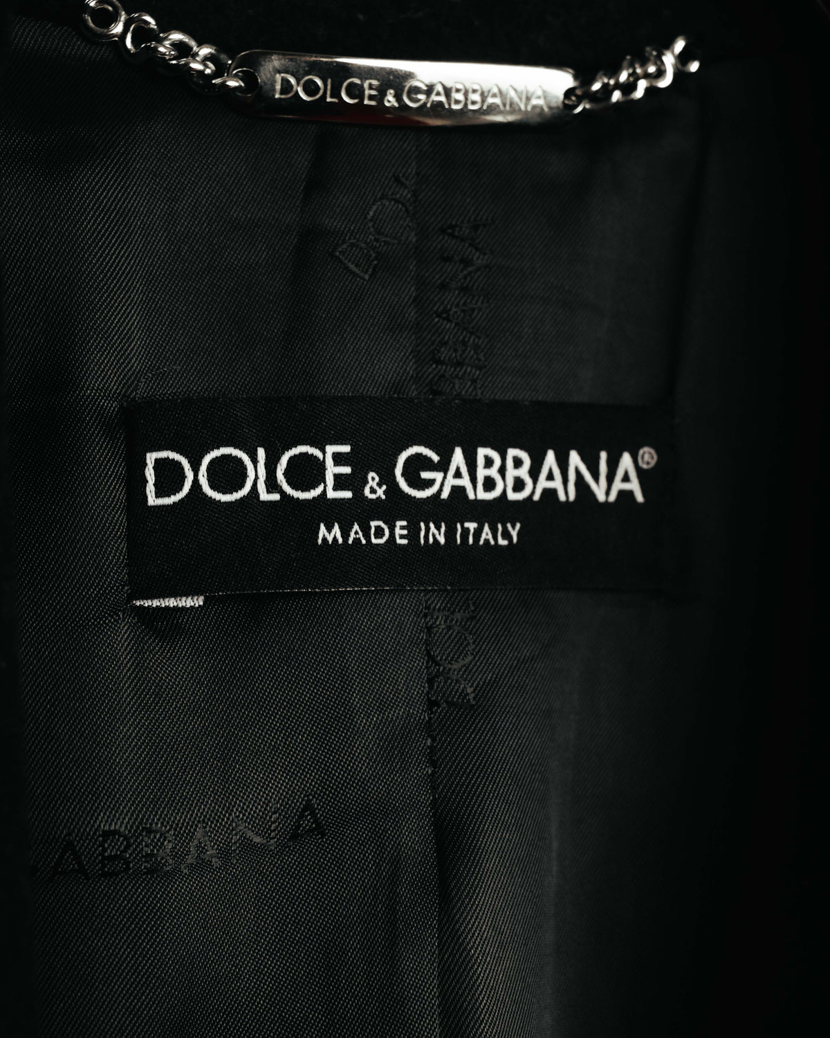 内側に配された、DOLCE & GABBANAのブランドネーム刻印入りメタルチェーンハンガーループと「MADE IN ITALY」表記の首元織りタグ。総裏地にはブランドネームを織り込んだジャカード柄が確認できます。