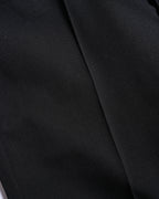 漆黒のウールギャバジン調生地と、縦のラインを描くセンタークリースを捉えた素材アップ。細かな織り目と滑らかな表面感が確認できます。