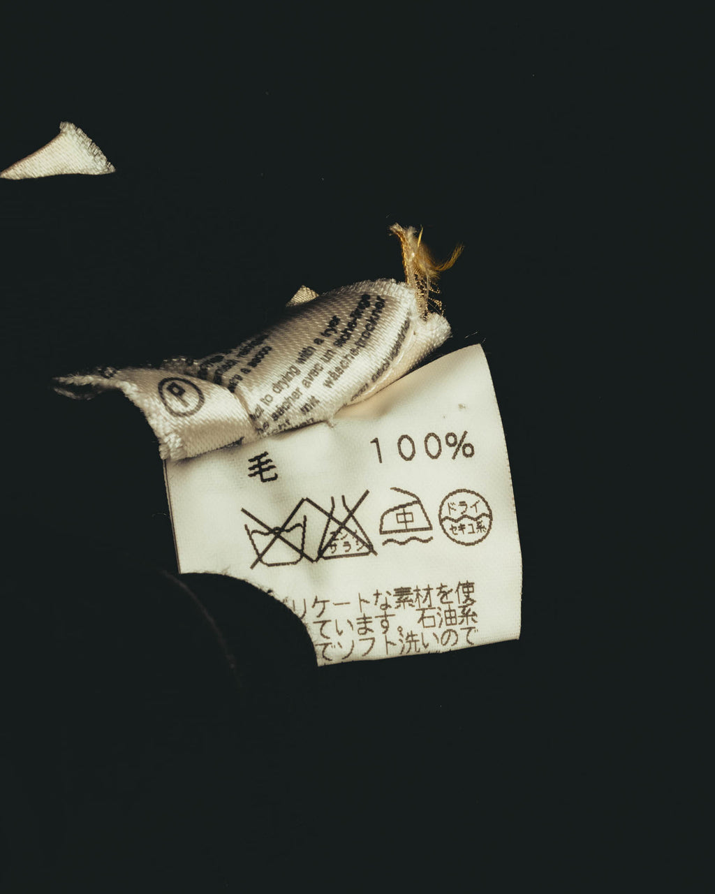 旧JIS系の洗濯表示と「毛 100%」表記を確認できる日本語品質表示タグのカット。内側にはイタリア製表記を含む織りタグが重なっている。